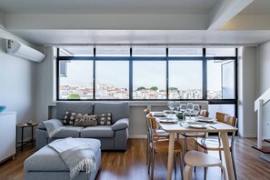 Ein moderner Wohnraum mit einer Couch, einem Esstisch und Stühlen, großen Fenstern mit Stadtblick und einem kleinen Beistelltisch.