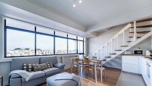 Un apartamento moderno con comedor, sofá, reposapiés, cocina y una escalera.
