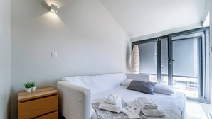 Un dormitorio moderno con una cama, mesitas de noche, una planta pequeña y una ventana con persianas.
