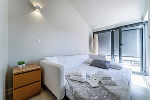 Ein modernes Schlafzimmer mit Bett, Nachttischen, einer kleinen Pflanze und einem Fenster mit Jalousien.