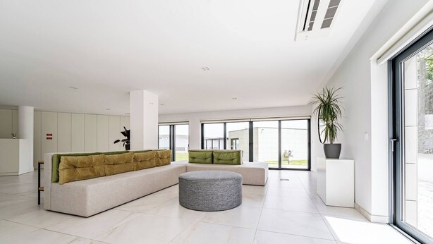 Een modern interieur met een hoekbank, een rond voetenbankje en een potplant.