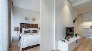 Een moderne hotelkamer met een bed, nachtkastje, lamp, televisie en kitchenette.