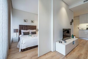 Ein modernes Hotelzimmer mit Bett, Nachttisch, Lampe, Fernseher und Küchenzeile.