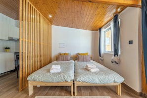 A room with two beds, wooden ceiling, a window with curtains, and a kitchenette in the background. - Wake up with the Sea Breeze- House with pool AP2 (Lavra)
