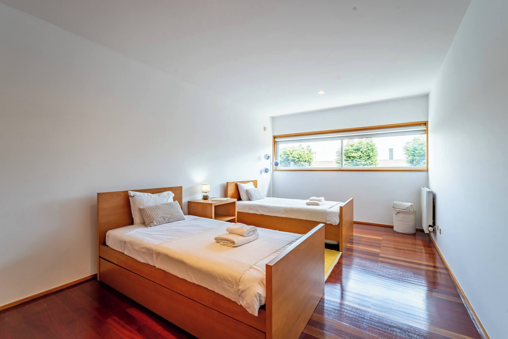 Een slaapkamer met een groot bed, een kleiner bed, een raam en een radiator.