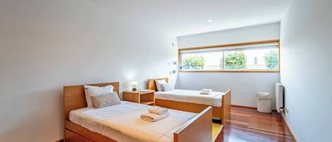 Een slaapkamer met een groot bed, een kleiner bed, een raam en een radiator.