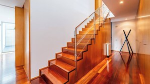 Una escalera moderna con escalones de madera y barandillas de vidrio, que sube a un nivel superior.