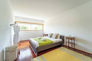 Un dormitorio con una cama, una mesita de noche, una ventana y un perchero.