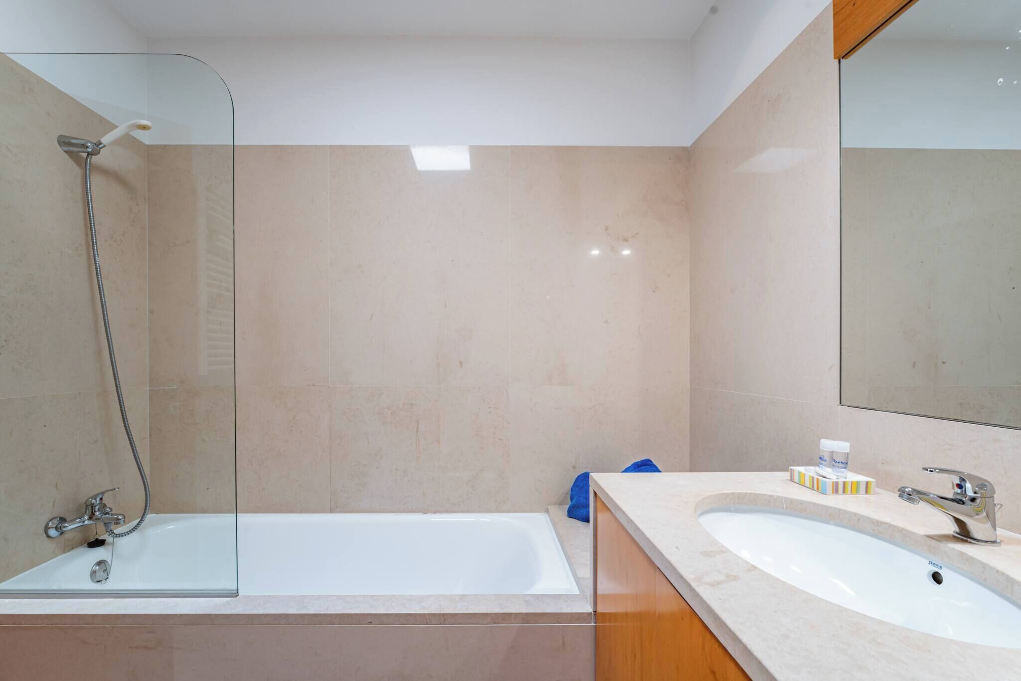 Ein modernes Badezimmer mit einer Glastrennwand zur Dusche, einer weißen Badewanne und einem Waschbecken mit Spiegel.