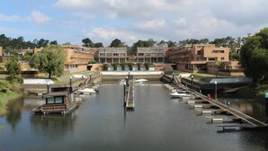 Una marina con barcos amarrados, un muelle central y edificios al fondo.