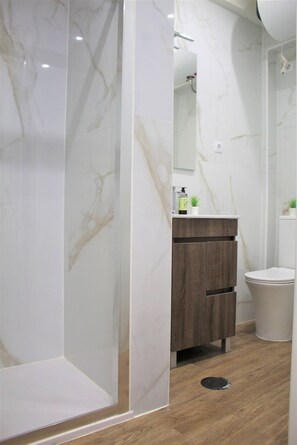 Ein Badezimmer mit Dusche, einem Holzkosmetikschrank, einer Toilette und einer Marmorwand.
