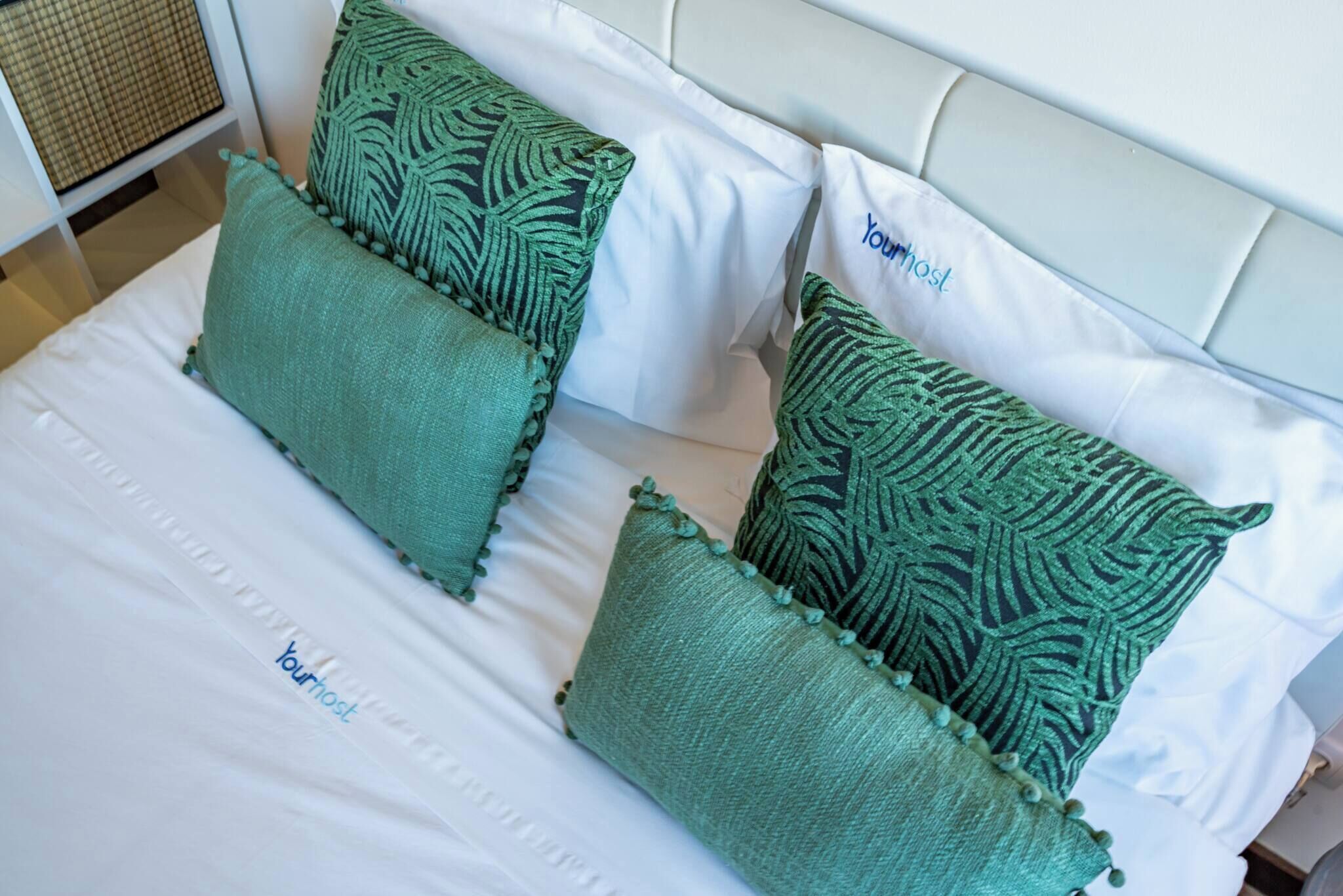 A bed with white bedding and green pillows with tassels.