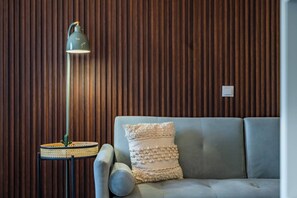 A room with a wooden slatted wall, a grey sofa with a textured cushion, and a floor lamp with a round base. - Plan C Downtown Apartment (Oporto)