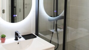 A modern bathroom with a glass-enclosed shower, a white sink with a black faucet, and a mirror with a circular light. - Valbom Hideaway Light, Style and Peace (Valbom)