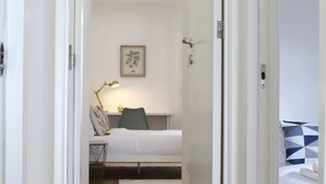 A narrow hallway leading to a bedroom with a bed, a bedside table, and a lamp. - Valbom Hideaway Light, Style and Peace (Valbom)