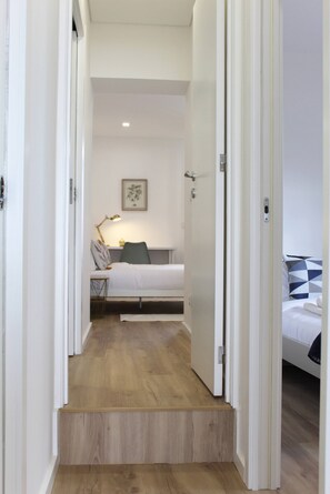 A narrow hallway leading to a bedroom with a bed, a bedside table, and a lamp. - Valbom Hideaway Light, Style and Peace (Valbom)