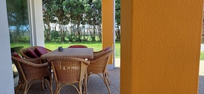 A wicker table and chairs set in a covered outdoor area with a view of trees and a building in the background. - Wake up with the Sea Breeze- House with pool AP1 (Lavra)