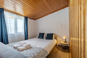 A bedroom with a wooden ceiling, a bed with white linens, two pillows, a bedside table with a lamp, and a window with curtains. - Wake up with the Sea Breeze- House with pool AP1 (Lavra)