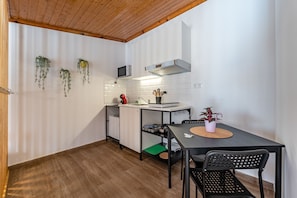 A compact kitchen with a wooden ceiling, white walls, a microwave, a sink, a small refrigerator, a dining table with chairs, and hanging plants. - Wake up with the Sea Breeze- House with pool AP1 (Lavra)