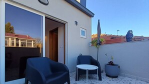 Un patio con dos sillas y una mesa pequeña, una planta en maceta y una estatua en la pared.