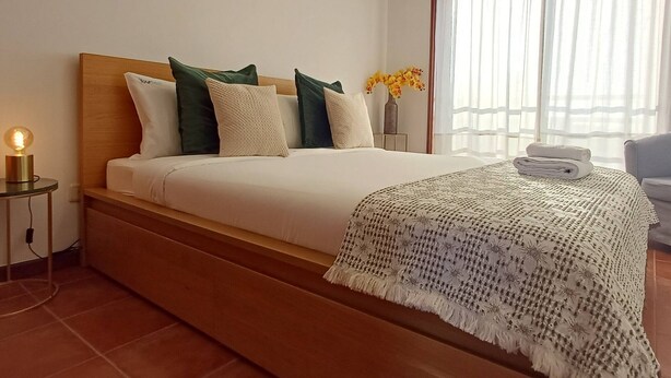 Una cama bien tendida con almohadas, una lámpara de noche y una colcha.