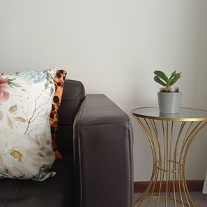 A dark leather sofa with a floral pillow, a small potted plant on a gold wire table, and a plain wall. - Perfect Oporto with Terrace and Good Vibes (Oporto)