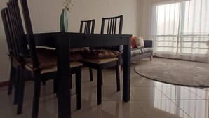 Un comedor con una mesa, sillas, un florero con flores, un sofá y un amplio ventanal con cortinas.