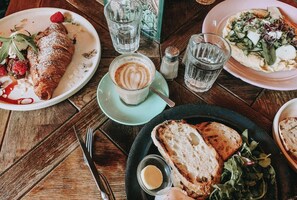 Ein Tisch mit Speisen, darunter ein Croissant, Kaffee, Brot und ein Salat.