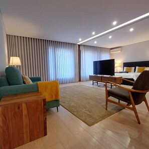 Ein modernes Hotelzimmer mit Sofa, Sessel, Fernseher und einem Bett mit Kopfteil.