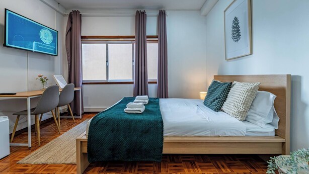 Une chambre à coucher avec un lit, un bureau, des chaises, une télévision et une fenêtre avec des rideaux.