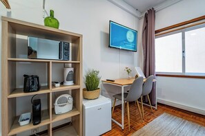Ein Zimmer mit einer Holzhülle, einem kleinen weißen Kühlschrank, einem Schreibtisch mit Stuhl, einem an der Wand montierten Fernseher und einem Fenster mit Vorhängen.