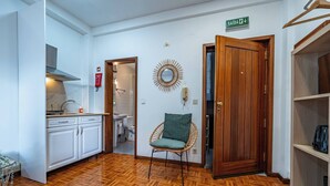Une pièce avec un parquet en chevrons, une chaise en osier, une porte en bois et un miroir au mur.