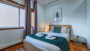 Une chambre d’hôtel avec un lit, une fenêtre avec des rideaux, un tableau encadré au mur et une petite table d’appoint avec une plante.