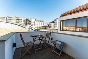 Ein Balkon mit Tisch und Stühlen, ein kleiner Tisch mit einer Zeitschrift und Blick auf Gebäude im Hintergrund.