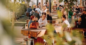 Ein Straßencafé mit Tischen und Stühlen, umgeben von viel Grün.
