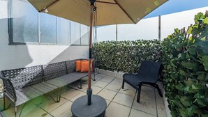 Un patio con un banco de metal, una mesa redonda y un paraguas grande.