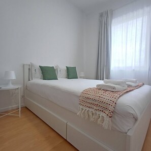 A single-bed room with a white bed, green pillows, a white bedside table with a lamp, and a window with curtains. - Your Home in Porto 1480 Style and Confort (Oporto)