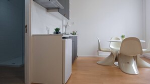 Ett modernt kök med en inbyggd diskmaskin, ett vitt kylskåp och en grå köksfläkt. Det finns en matplats med ett vitt bord och stolar, och en liten krukväxt på bordet.