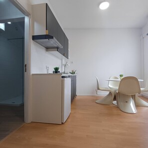 A modern kitchen with a built-in dishwasher, a white refrigerator, and a grey range hood. There is a dining area with a white table and chairs, and a small potted plant on the table. - Your Home in Porto 1480 Style and Confort (Oporto)