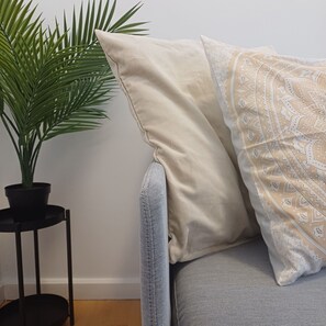 A corner of a room with a grey sofa, a beige pillow, a patterned pillow, and a potted plant on a small black table. - Your Home in Porto 1480 Style and Confort (Oporto)