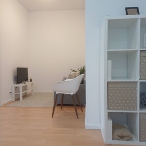 A living room with a white chair, a TV on a stand, a bookshelf, and a small plant. - Your Home in Porto 1480 Style and Confort (Oporto)