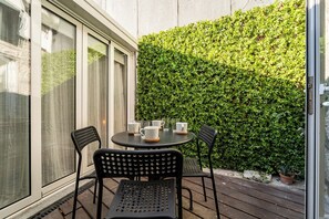 Un patio con una mesa redonda y sillas, una puerta de vidrio y un muro de seto verde.