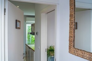 Ein Flur mit einer Tür zu einem Zimmer, einem Spiegel mit gewebtem Rahmen und einer Topfpflanze.