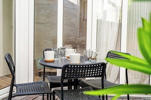 Eine Terrasse mit Tisch für vier Personen, umgeben von schwarzen Stühlen und einem Glasabtrenner im Hintergrund.