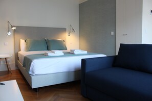 Ein Hotelzimmer mit Bett, Nachttischlampen, einem Sessel und einem Schreibtisch.