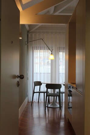 Ein Zimmer mit Esstisch, zwei Stühlen, einer Pendelleuchte und Blick durch ein Fenster mit durchsichtigen Vorhängen.