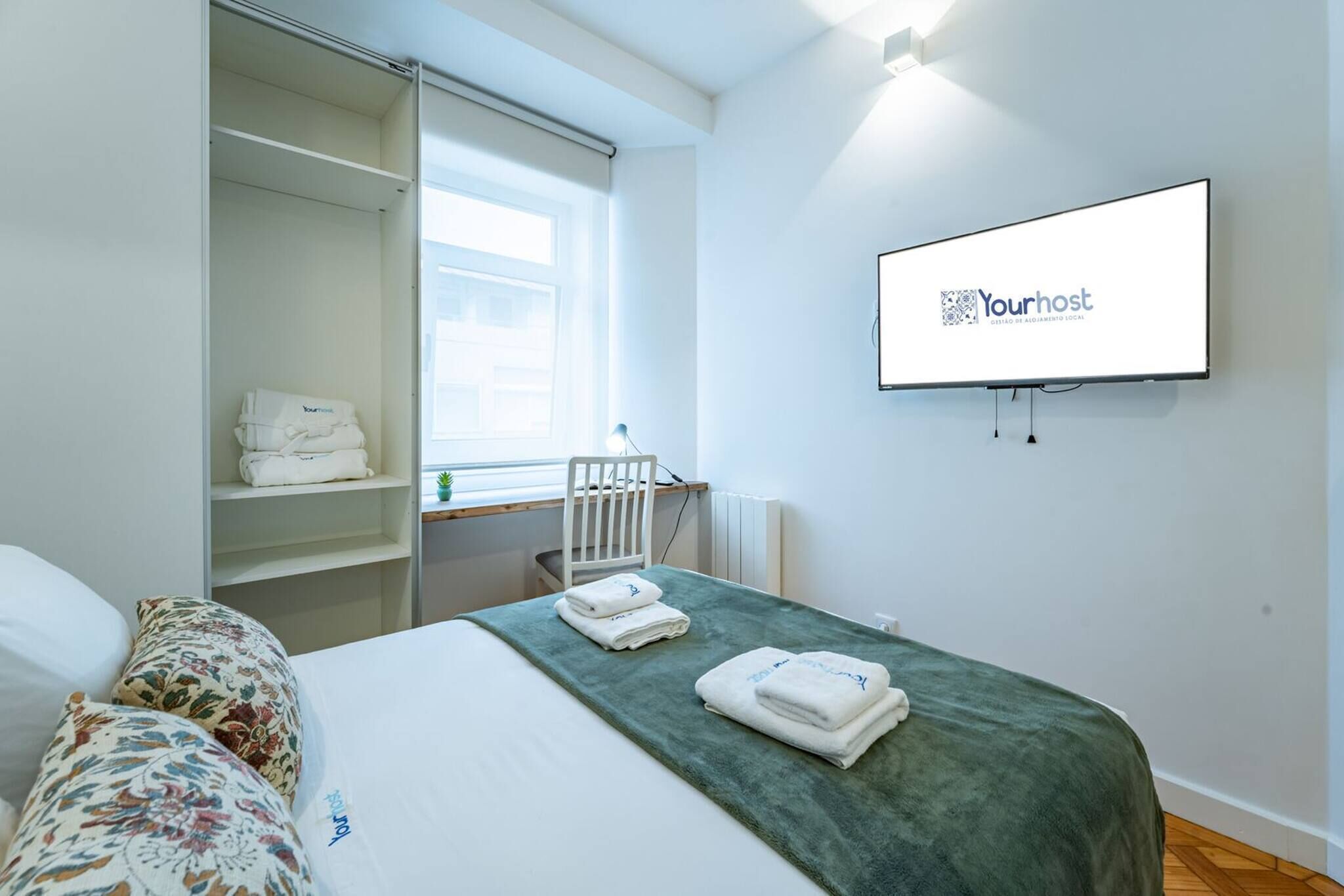 Hotellihuone, jossa on sänky, seinälle asennettu televisio, vaatekaappi ja ikkuna.