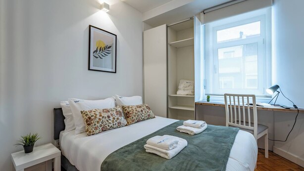 Ein Schlafzimmer mit Bett, Nachttisch, Schreibtisch, Stuhl und einem Fenster.