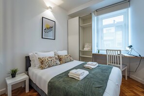 Camera da letto con un letto, comodino, scrivania, sedia e una finestra.