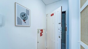 Ein Flur mit einem gerahmten abstrakten Kunstwerk, einer Tür mit einem Notausgangsschild und einer strukturierten Wandverkleidung.
